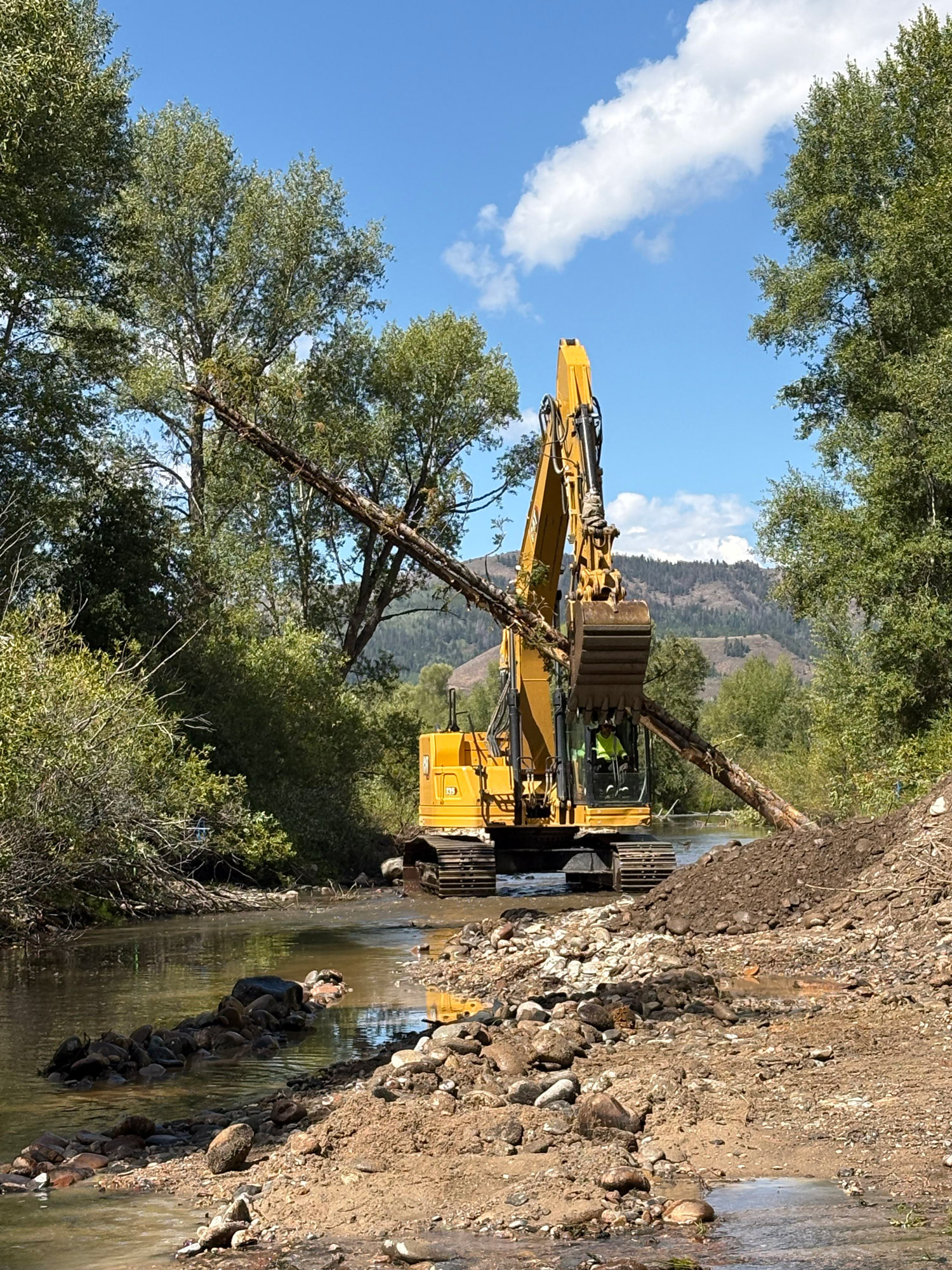 Kaibab Park Stream Restoration A large construction vehicle pulling a dead tree a stream
